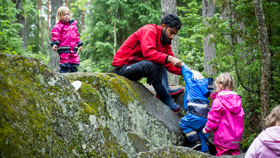 Lärare hjälper barn att klättra i skogen.