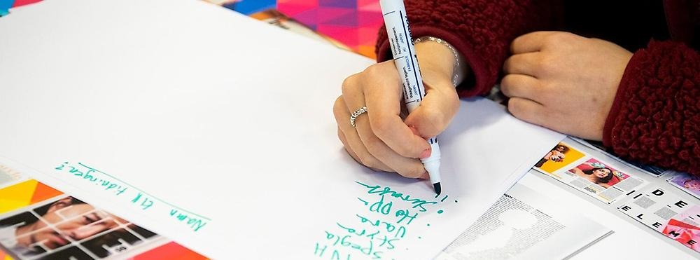 Student skriver med grön penna på ett vitt papper