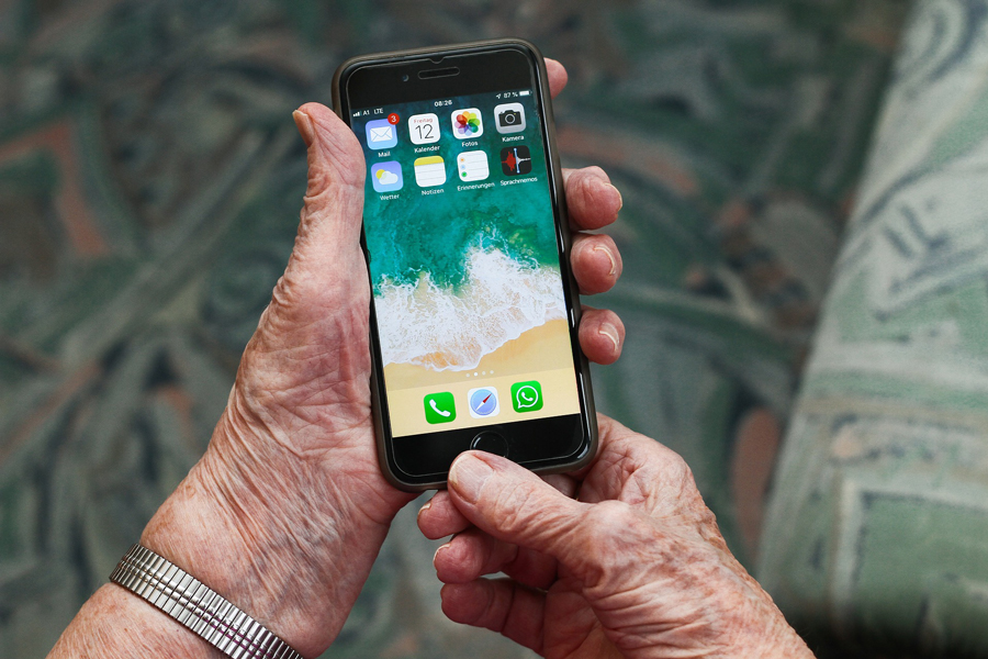 Händer på äldre person som håller i en mobiltelefon.