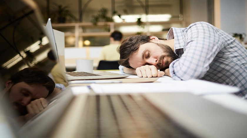 Man som sover lutad över sitt skrivbord framför sin skärm och tangentbord.